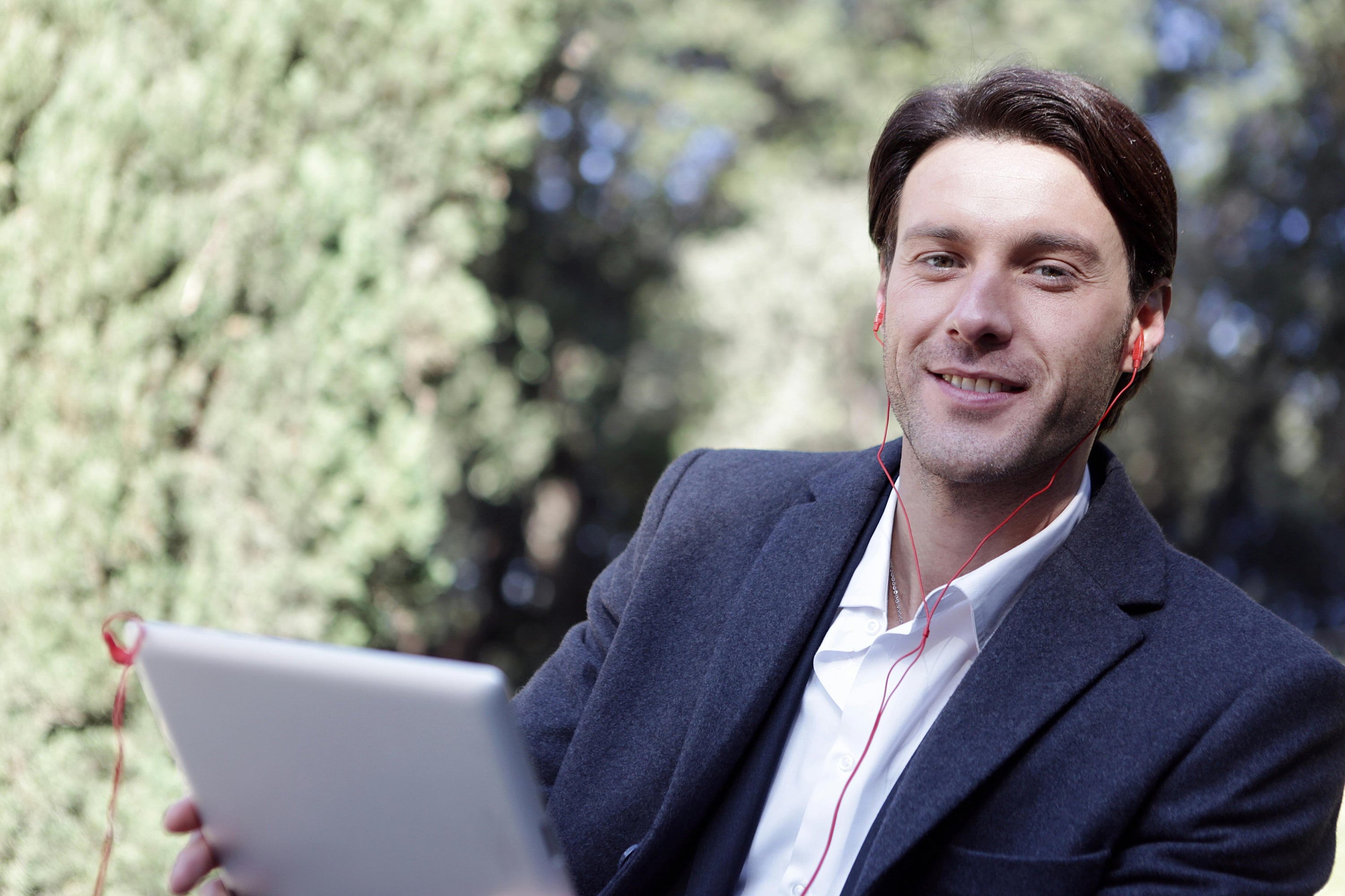 Man sitting outdoors with a tablet, wearing earphones